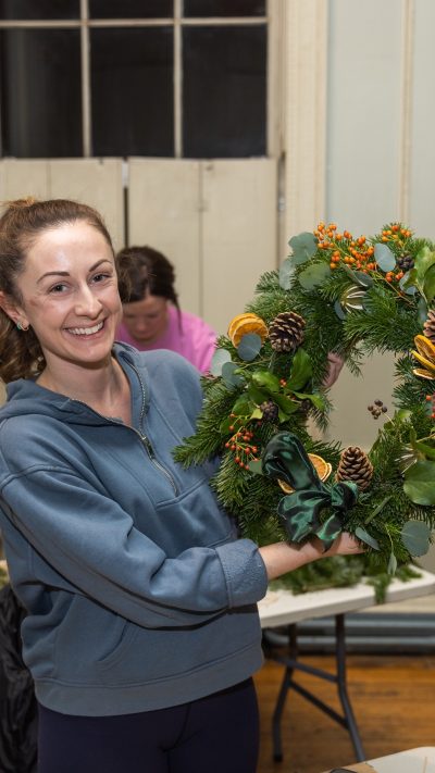 A woman holding a wreath that she has made at a Christmas wreath-making class