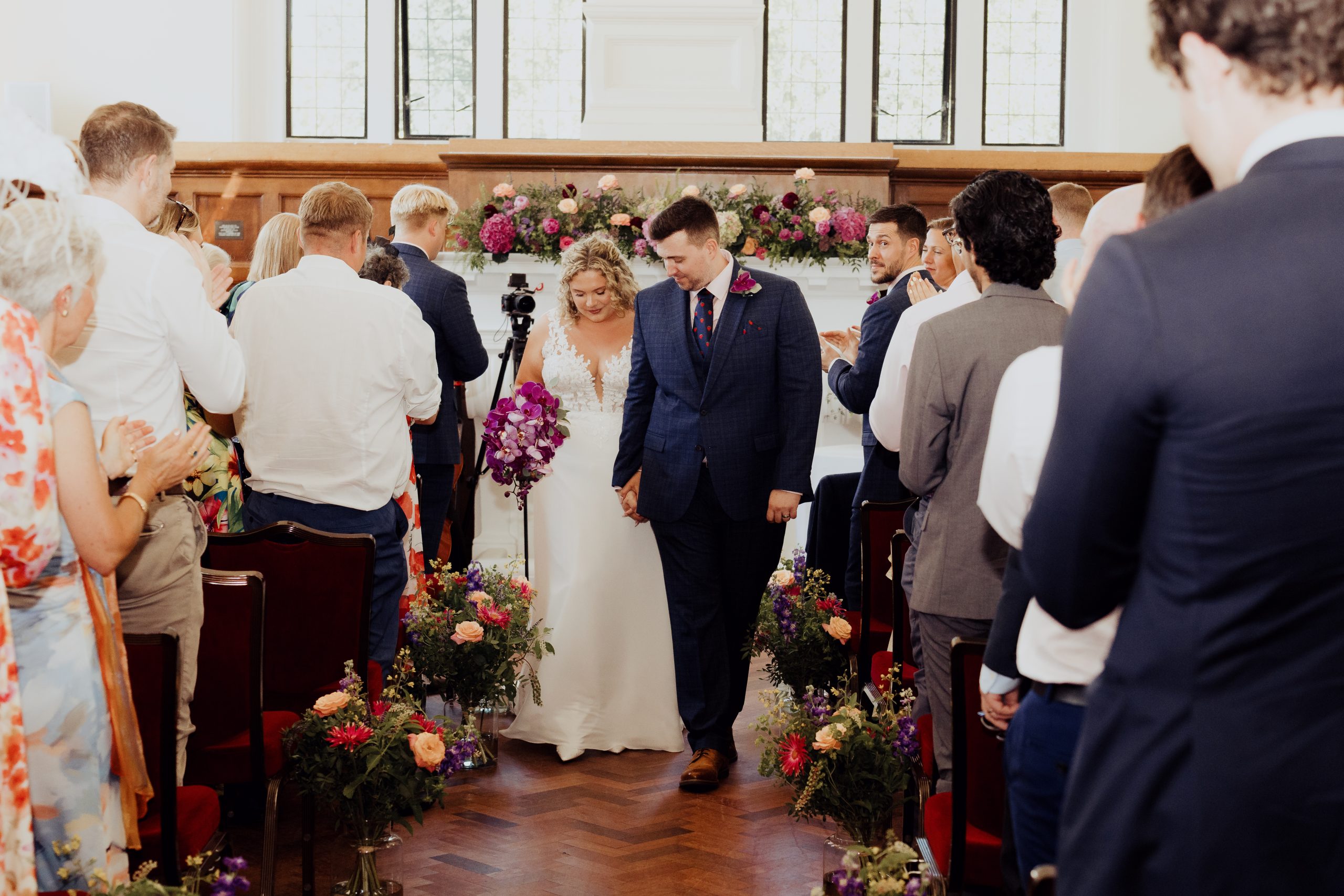 A newly married couple walking down the aisle at Dulwich College Chapel with Flowers by Just So Flowers