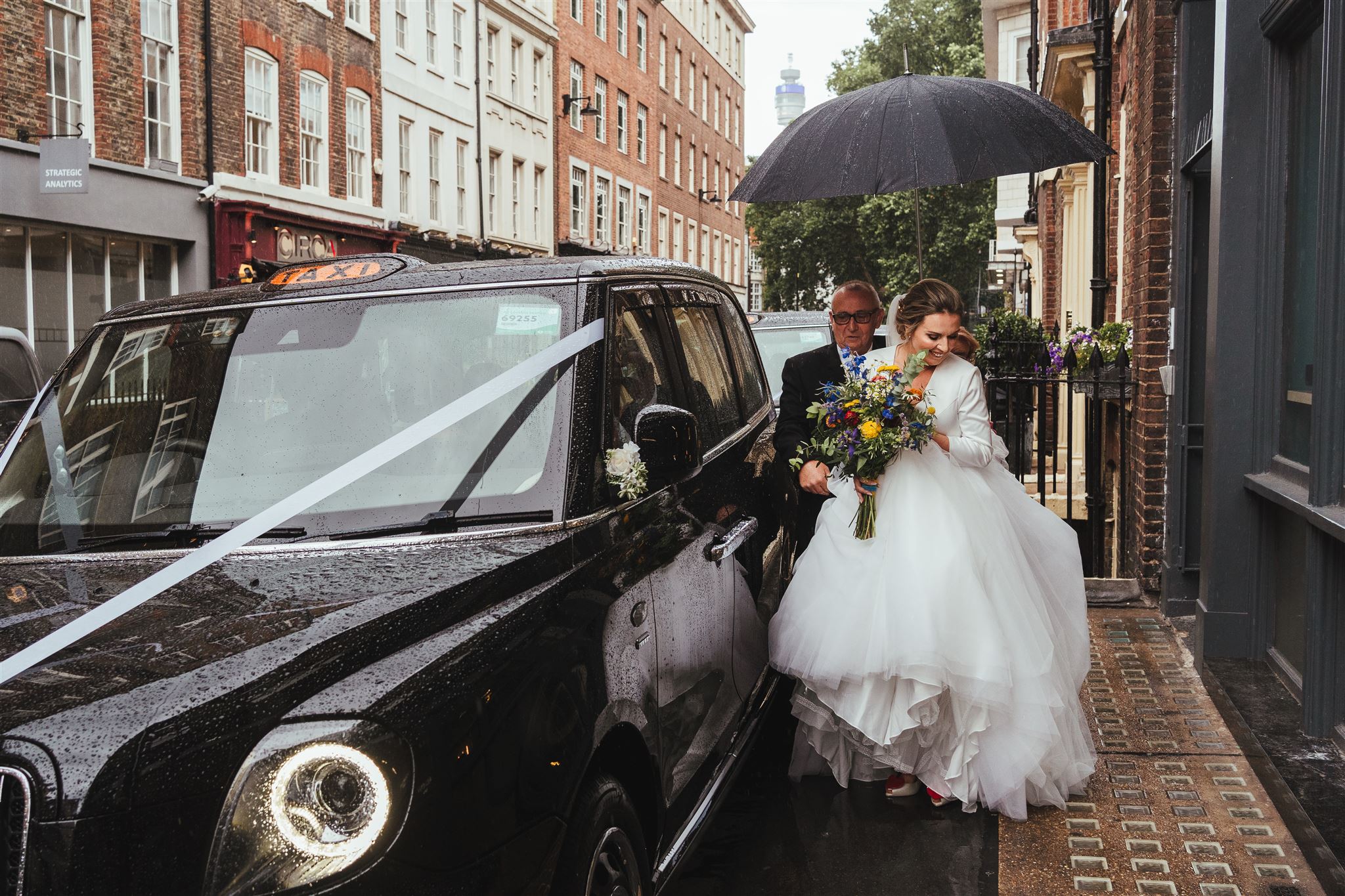 Bride getting out of a London taxi holding a bouquet by Just So Flowers