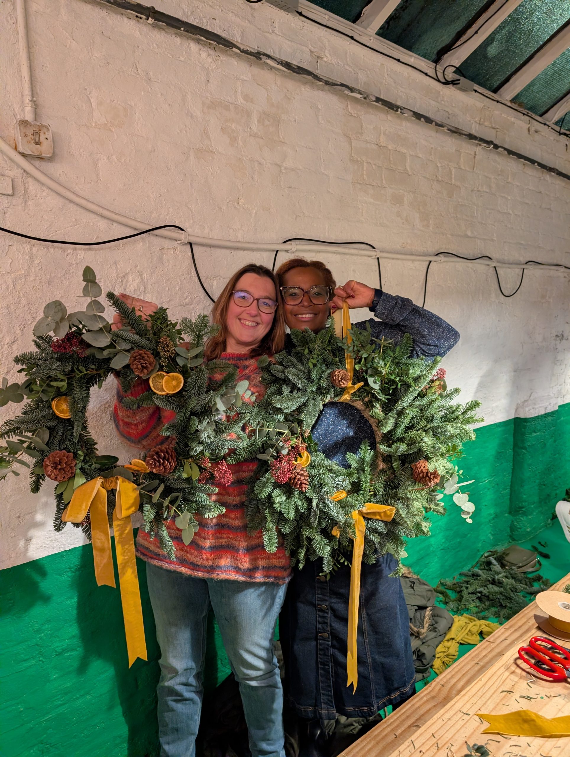 Two ladies holding their Christmas wreaths that they made at a workshop run by Just So Flowers